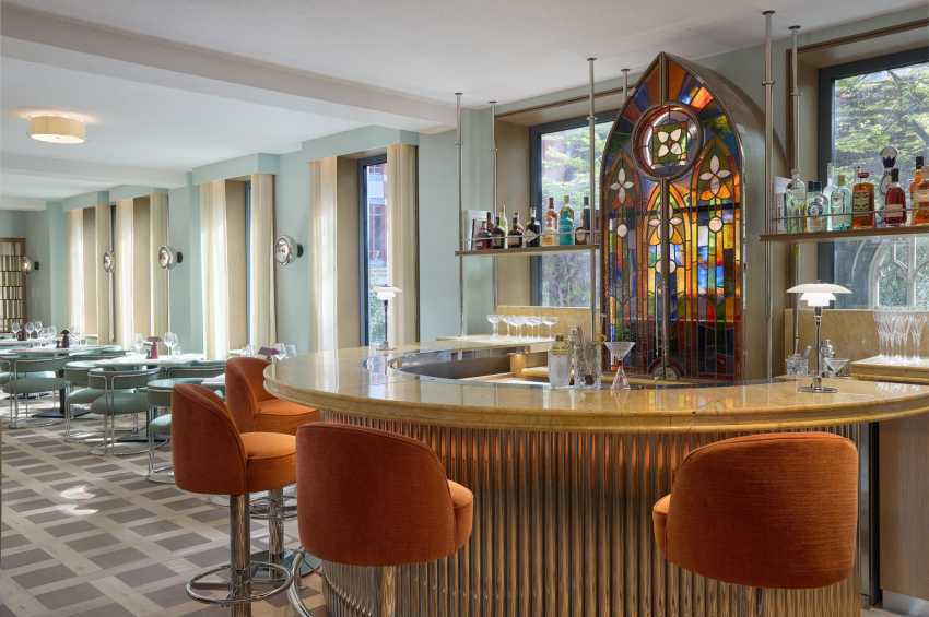 Private dining room with curved bar, orange bar stools, stained glass window, and seated dining area visible in background.