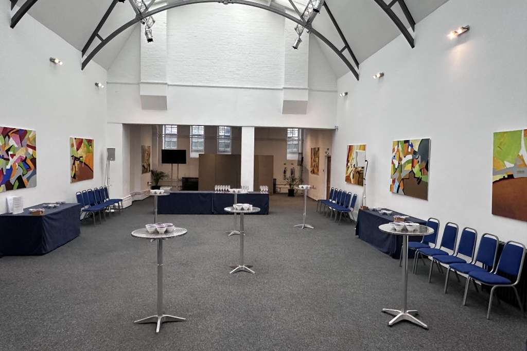 Mary Ward Hall with high vaulted ceiling, colorful artwork on walls, blue chairs, cocktail tables, and bar setup.