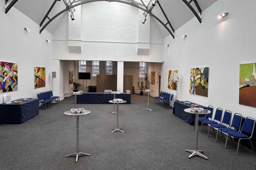 Mary Ward Hall with high vaulted ceiling, colorful artwork on walls, blue chairs, cocktail tables, and bar setup.