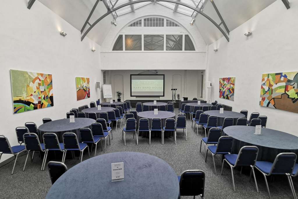 Mary Ward Hall set up for a conference with round tables, blue chairs, and projection screen under arched ceiling.