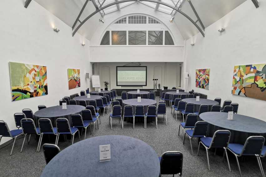 Mary Ward Hall set up for a conference with round tables, blue chairs, and projection screen under arched ceiling.