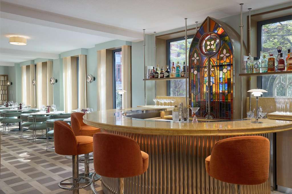 Private dining room with curved bar, orange bar stools, stained glass window, and seated dining area visible in background.