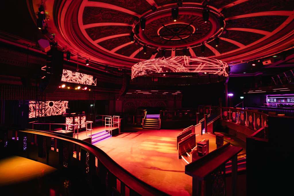 Modern event space with red and purple neon lighting, geometric ceiling design, elevated stage platform, and contemporary decor.