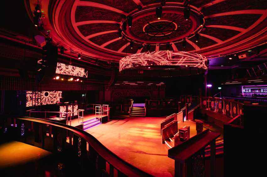 Modern event space with red and purple neon lighting, geometric ceiling design, elevated stage platform, and contemporary decor.