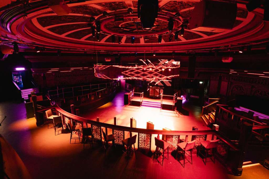 Modern venue interior with curved seating tiers, illuminated stage, and dramatic red and purple lighting throughout.