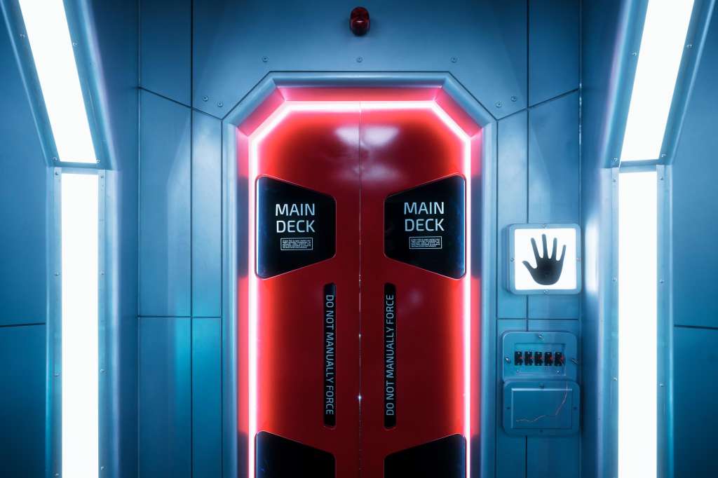 Modern corridor with neon-lit red doors labeled Main Deck and blue panel walls with industrial lighting.
