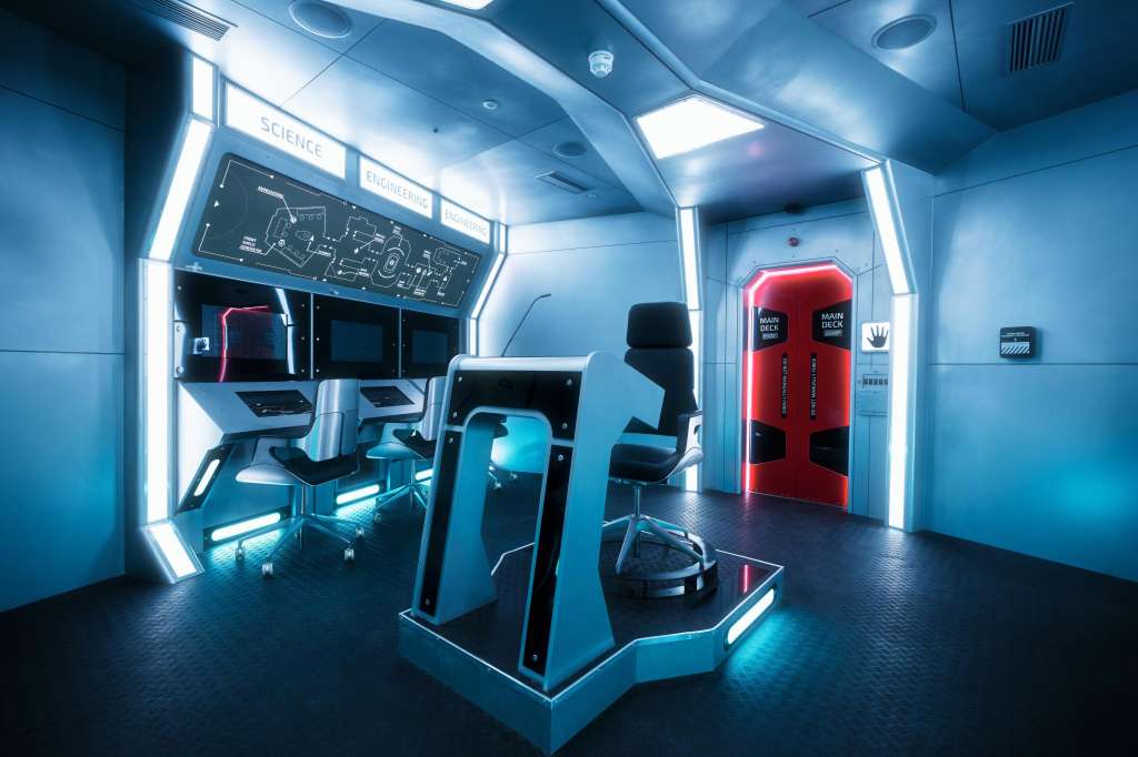 Futuristic control room with neon lighting, interactive stations, and red emergency doors.