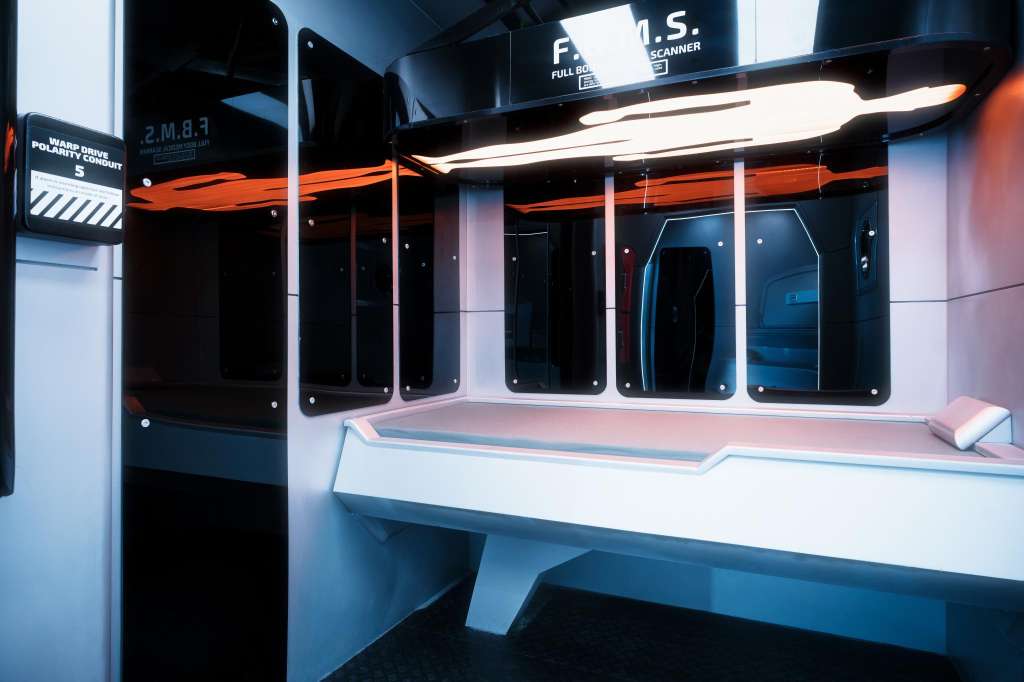 Modern interior with futuristic design, neon orange accents, illuminated signage, and sleek white counter with blue lighting.