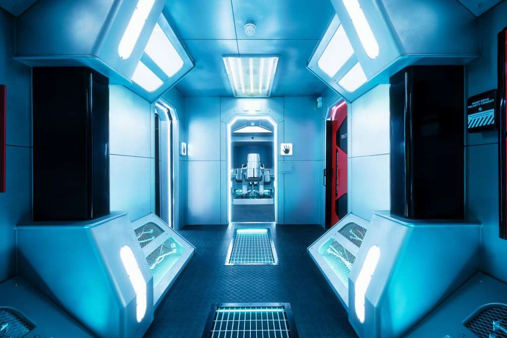 Futuristic corridor with blue lighting, metal grating floor, and modern architectural design.