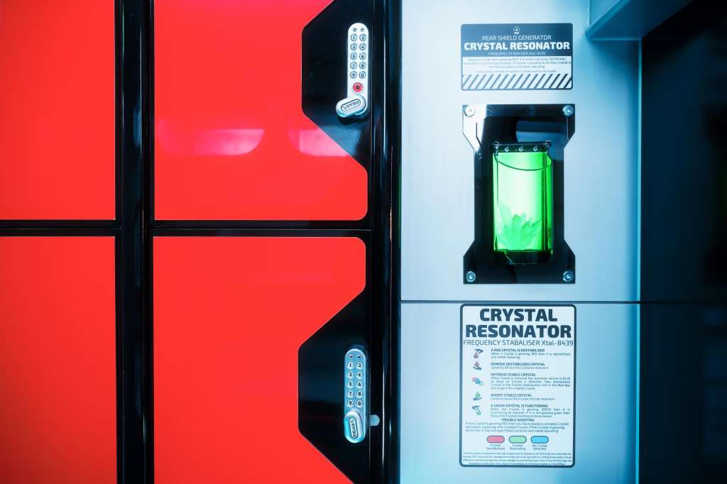 Close-up of a red door with digital keypad locks and a wall-mounted crystal resonator device with green illumination.