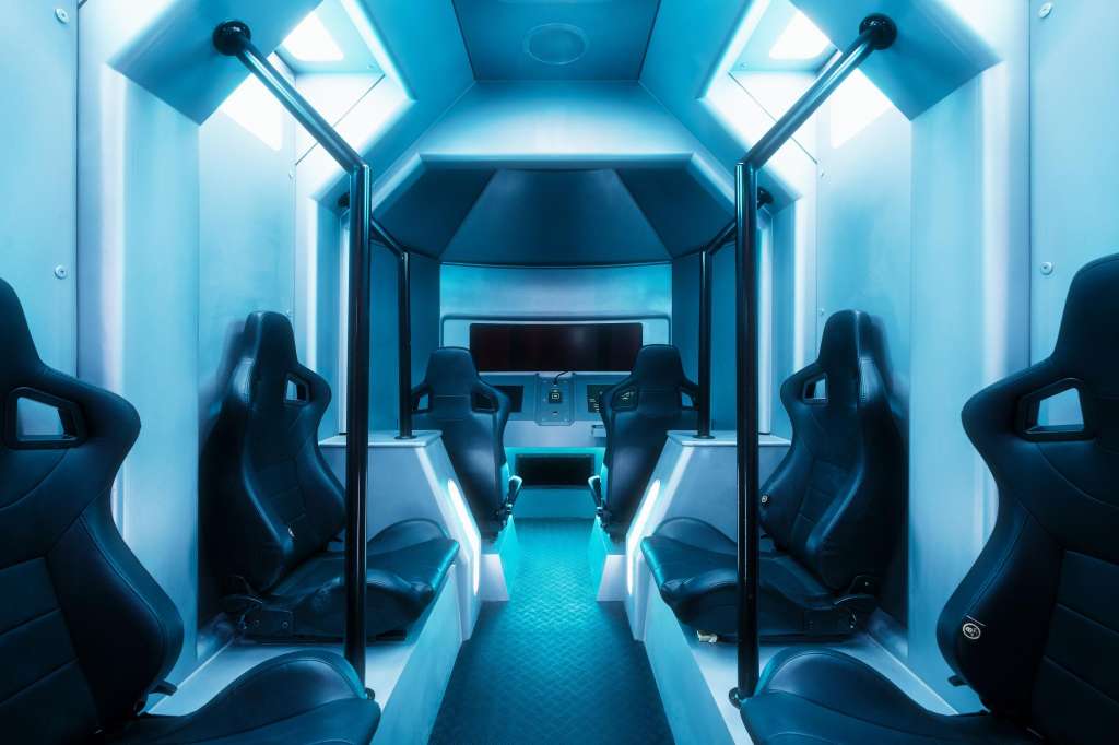 Interior of a futuristic vehicle or simulator with black racing seats, blue neon lighting, and a control console.