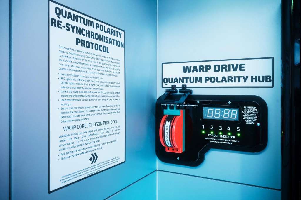 Close-up of a quantum polarity hub device with red and black components and digital display mounted on blue wall.