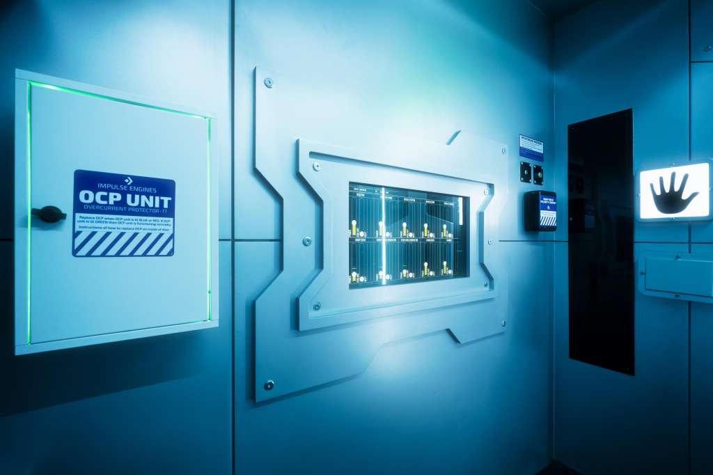 Modern exhibition space with illuminated display panels showing technical diagrams and branding on blue walls.