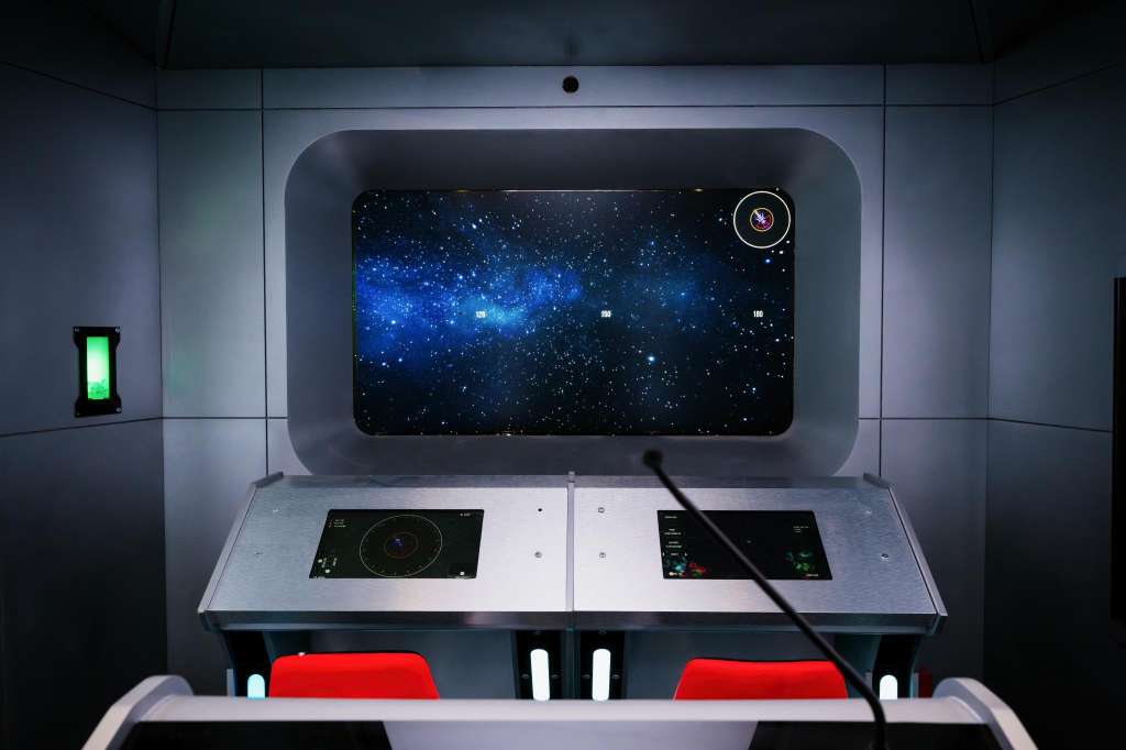 Interactive display console with starfield visualization on screen, control panels, and red seating visible below.