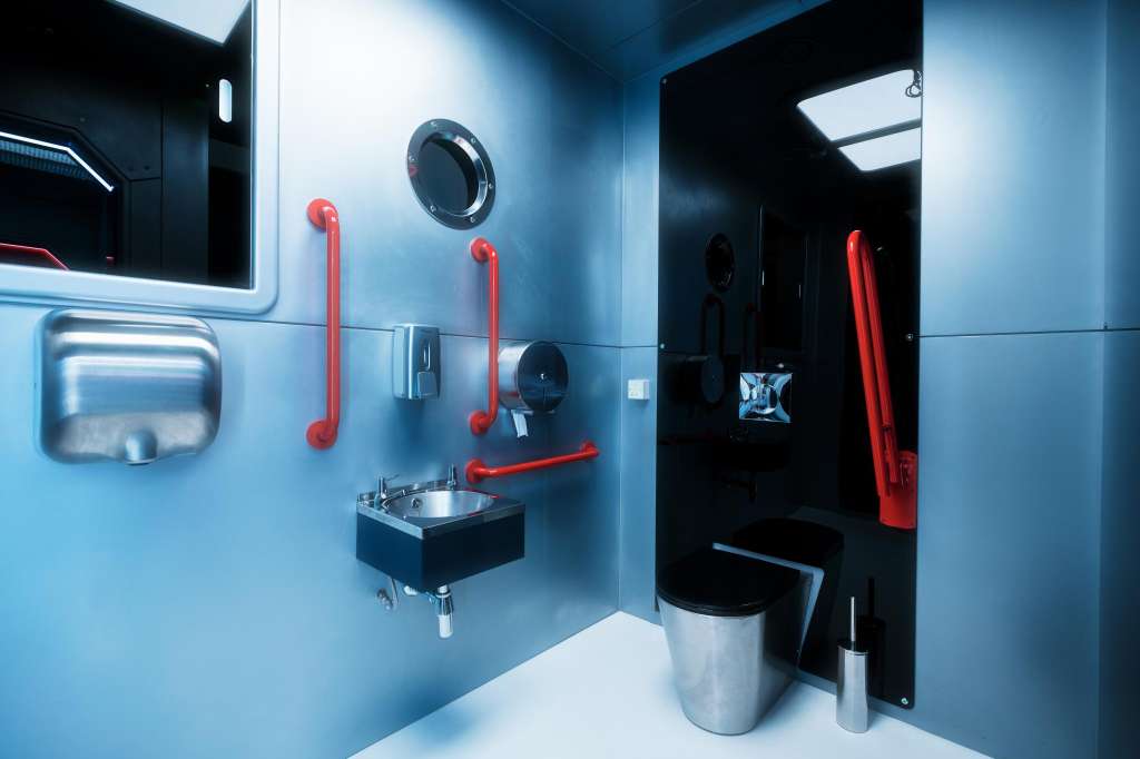 Modern bathroom with blue walls, red grab bars, stainless steel sink, and toilet.