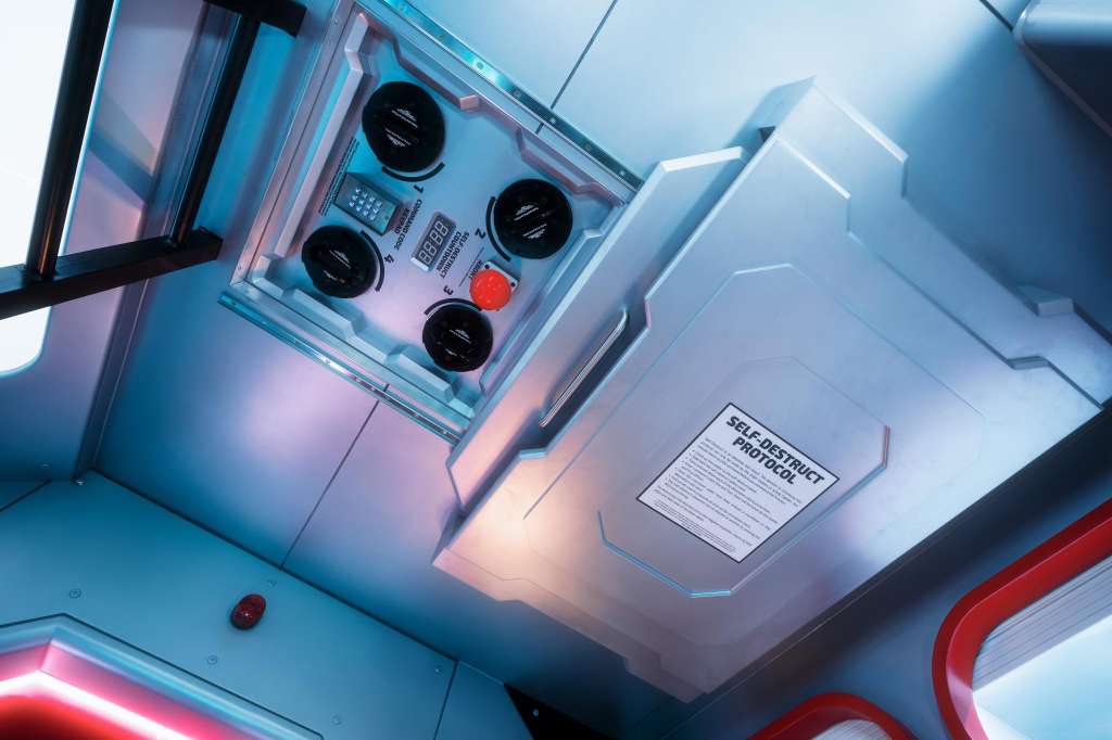 Control panel with four dials, red button, and illuminated display mounted on ceiling with blue and pink ambient lighting.