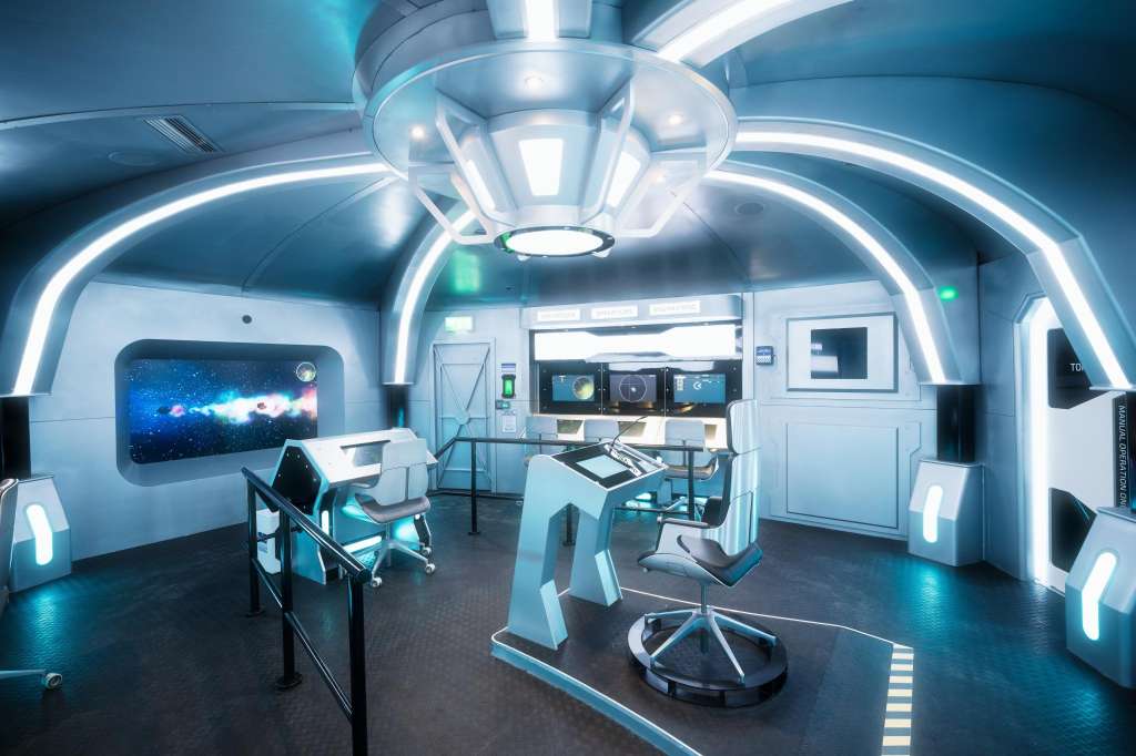 Futuristic control room with neon blue lighting, workstations, monitors, and sci-fi interior design.