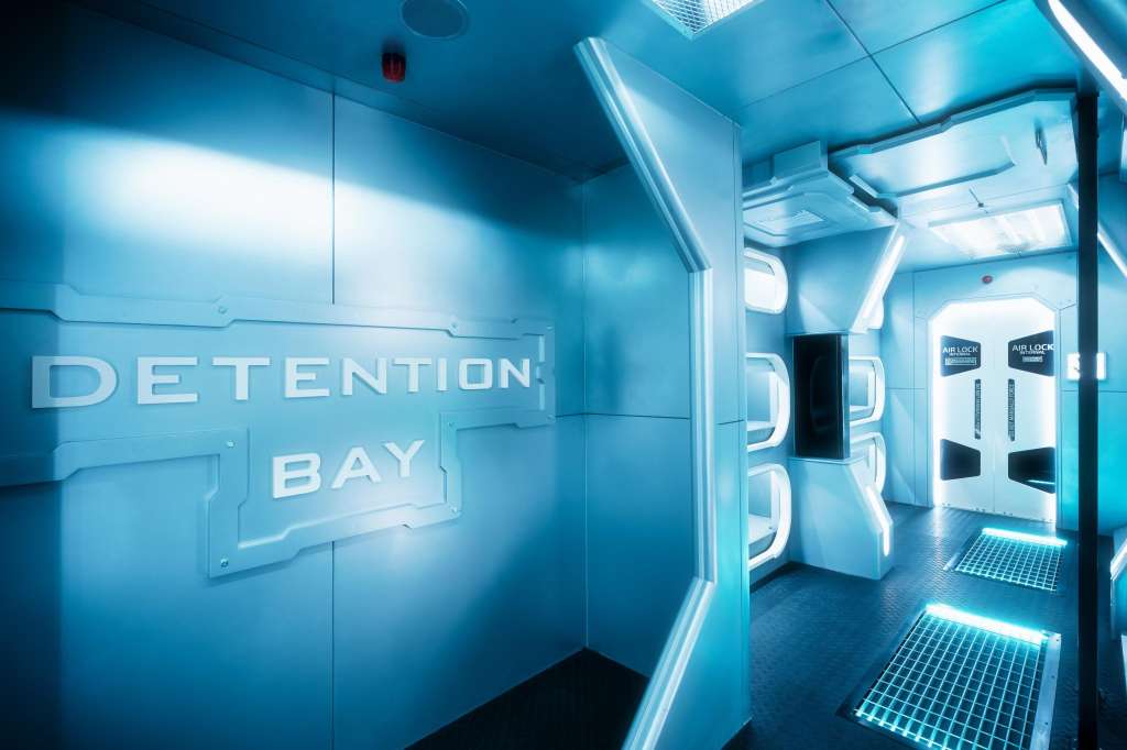 Futuristic corridor with blue neon lighting, white signage reading 'DETENTION BAY', and modern architectural features.