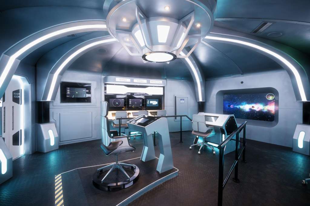 Futuristic control room with neon lighting, multiple screens, and workstations with modern chairs.