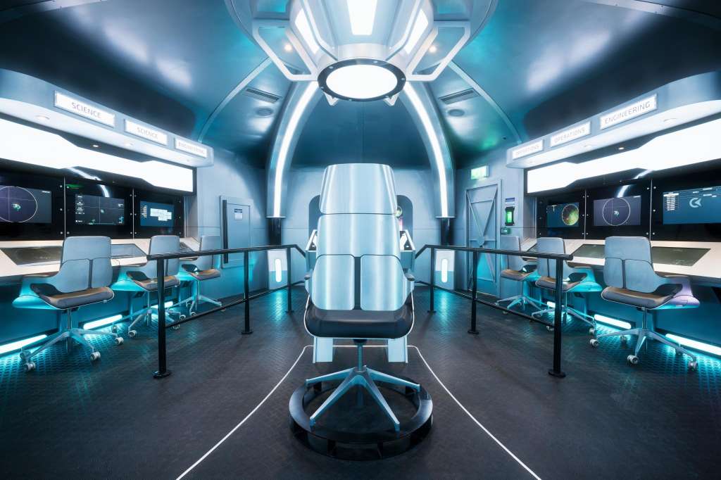 Futuristic control room with central command chair, monitoring stations, blue ambient lighting, and digital displays.