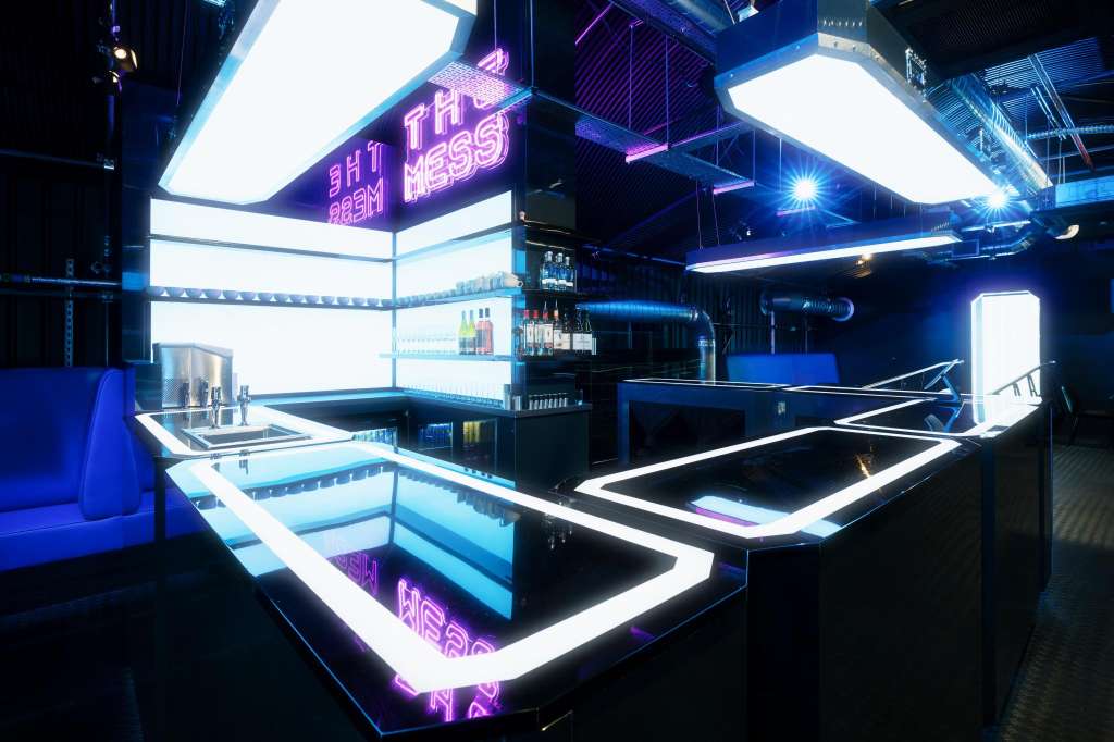 Modern bar interior with neon signage, illuminated shelving, geometric counter design, and blue ambient lighting.