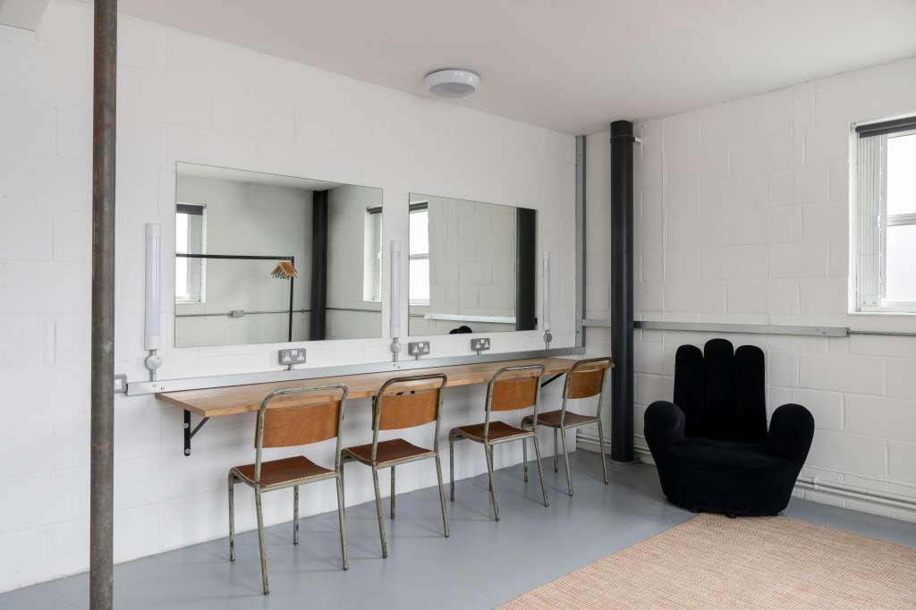 Modern studio space with vanity mirrors, wooden chairs, black sculptural seating, and polished concrete flooring.