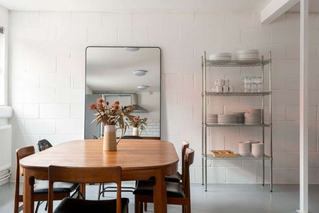 Modern dining space with round wooden table, mid-century chairs, white subway tile walls, and metal shelving unit.
