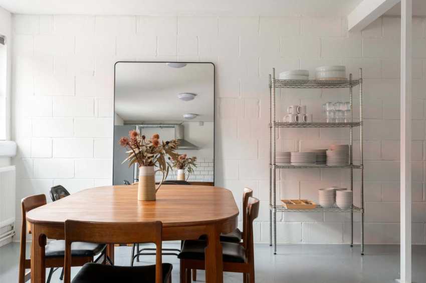 Modern dining space with round wooden table, mid-century chairs, white subway tile walls, and metal shelving unit.