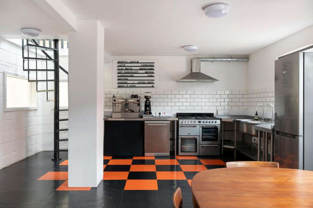 Modern kitchen with stainless steel appliances, white subway tile backsplash, orange and black checkered flooring, and menu board.