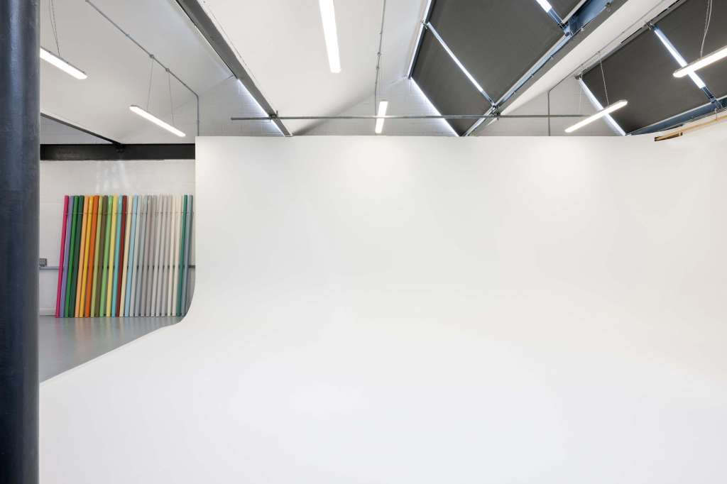 Minimalist gallery space with white walls, skylights, and colorful vertical panels leaning against wall.