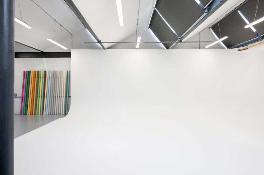 Minimalist gallery space with white walls, skylights, and colorful vertical panels leaning against wall.