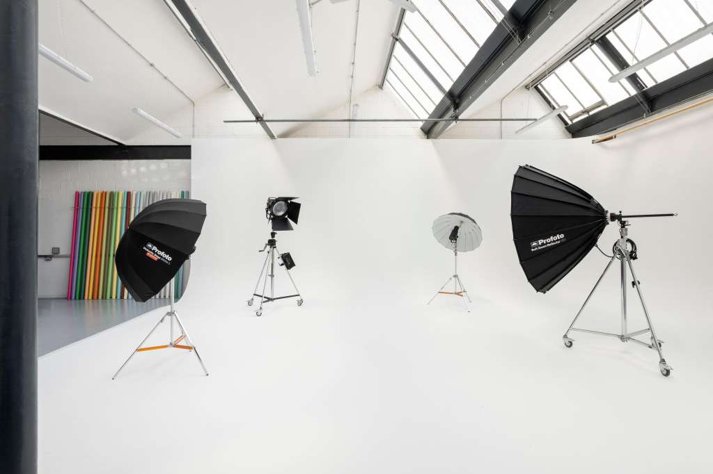 Photography studio with white walls, skylights, professional lighting rigs, and colorful backdrop panels.