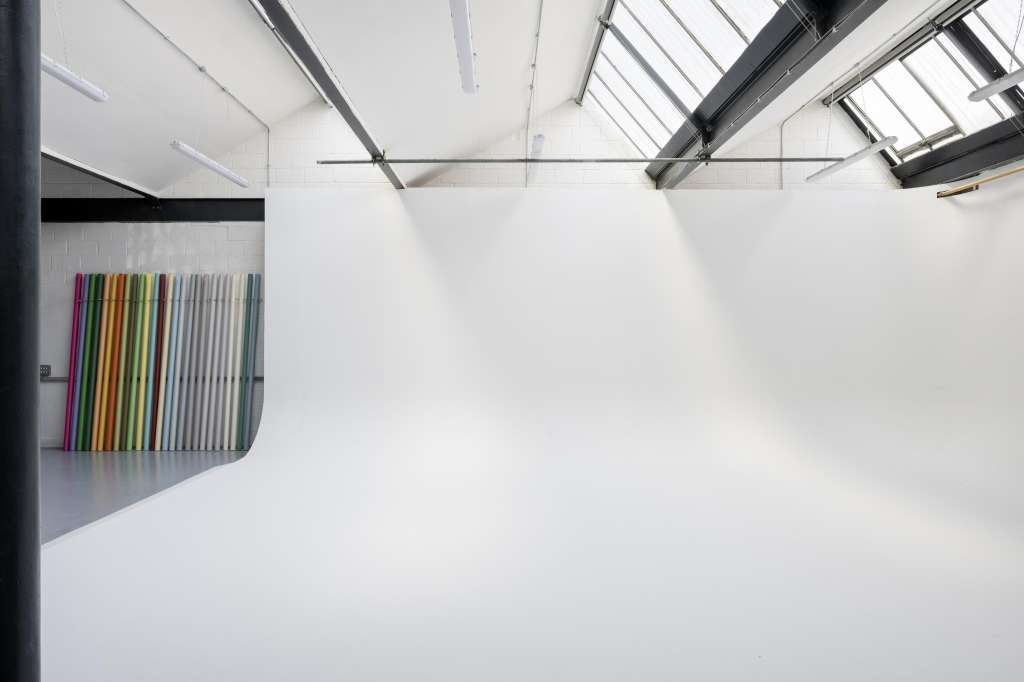 Bright industrial studio space with skylights, white walls, and colorful panel display on left wall.