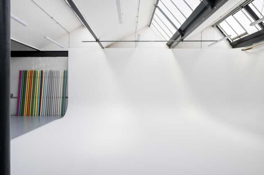 Bright industrial studio space with skylights, white walls, and colorful panel display on left wall.