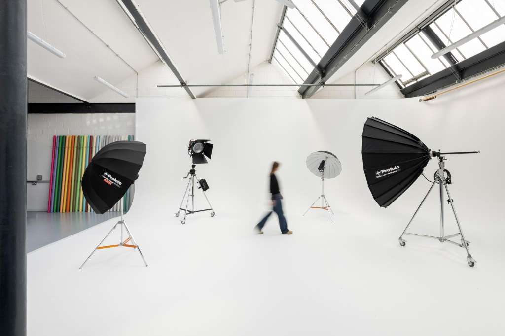 Photography studio with white walls, skylights, professional lighting rigs, and colorful backdrop panels.