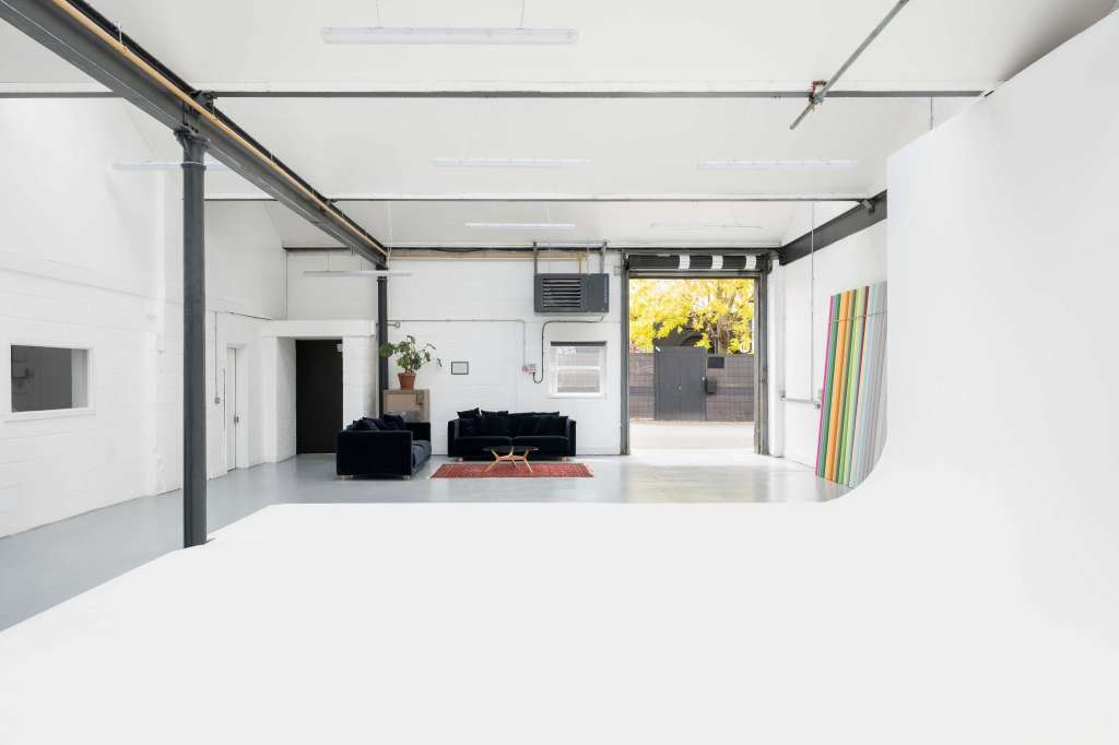Modern industrial space with polished concrete floor, exposed ductwork, black seating, and large windows showing autumn foliage.