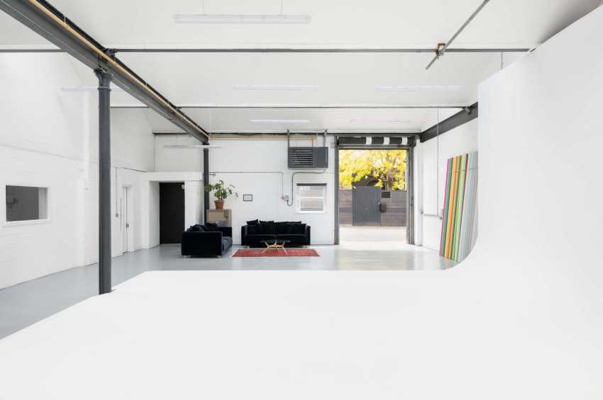 Modern industrial space with polished concrete floor, exposed ductwork, black seating, and large windows showing autumn foliage.