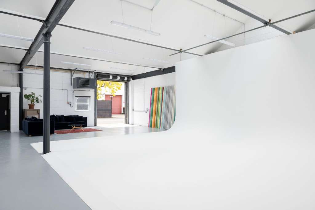 Industrial studio space with polished concrete floor, exposed beams, skylights, and open-plan layout with seating area.