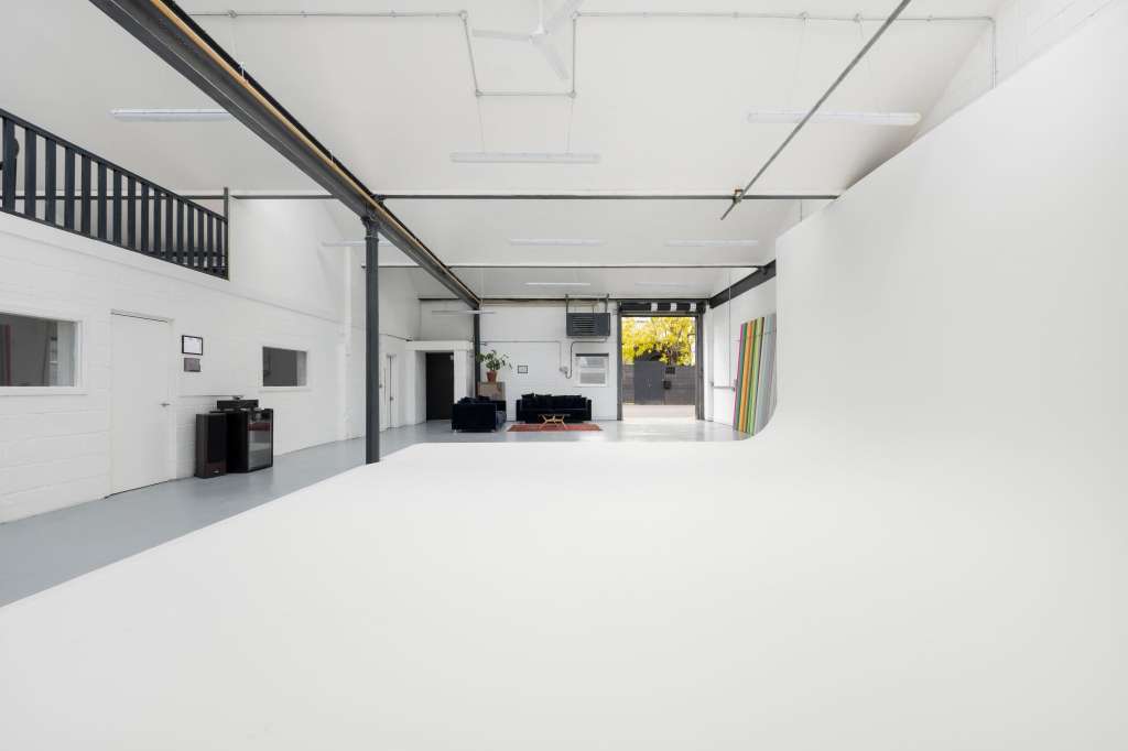 Modern industrial gallery space with polished concrete floor, white walls, exposed steel beams, and mezzanine level.