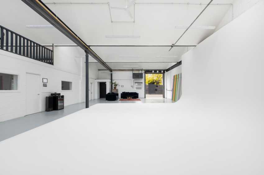 Modern industrial gallery space with polished concrete floor, white walls, exposed steel beams, and mezzanine level.
