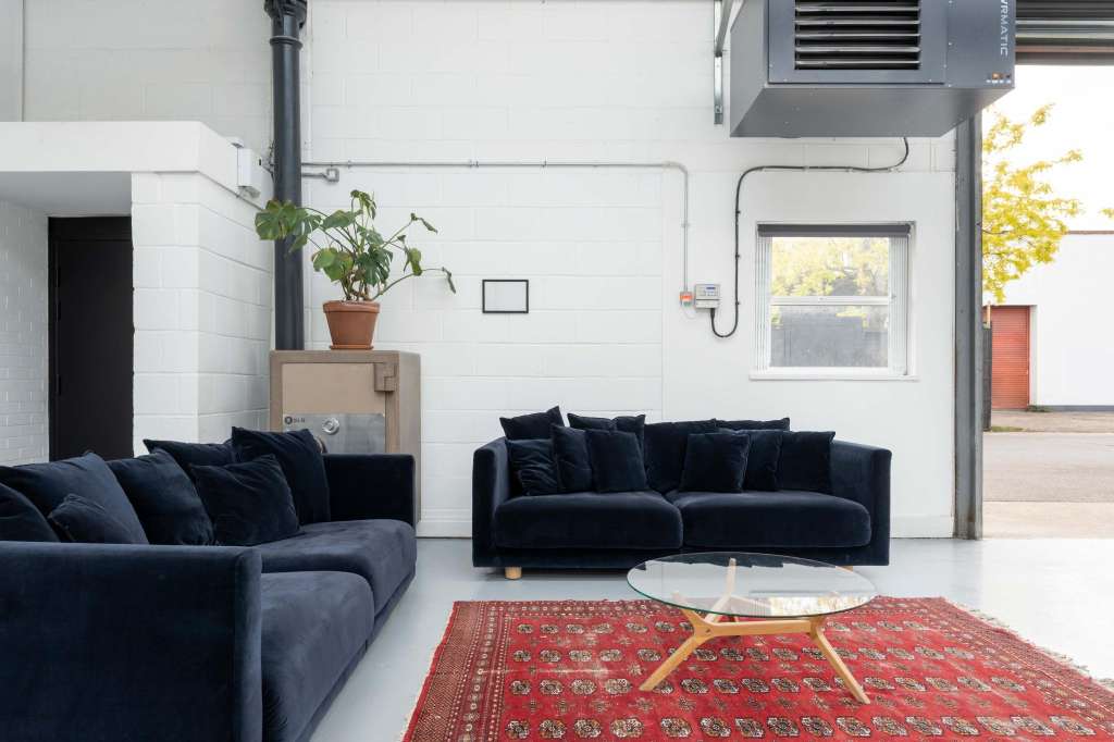 Modern lounge with dark blue sectional sofas, red patterned rug, round coffee table, and potted plant against white brick walls.