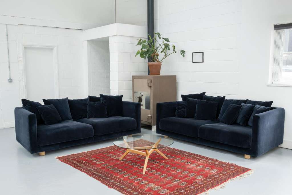 Modern lounge with two dark blue sofas facing each other across a glass table on a red patterned rug.