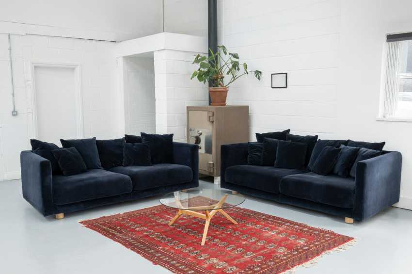 Modern lounge with two dark blue sofas facing each other across a glass table on a red patterned rug.