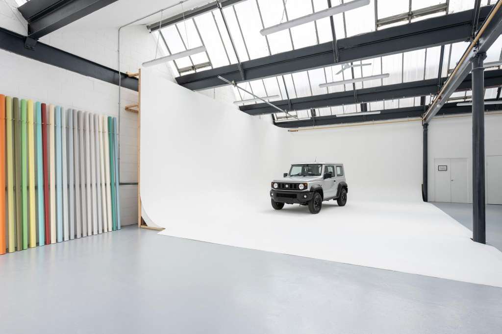 Industrial studio space with skylights, white floor, vehicle display, and colorful panel wall art.