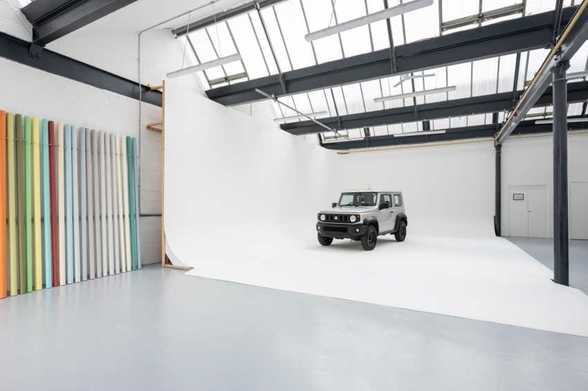 Industrial studio space with skylights, white floor, vehicle display, and colorful panel wall art.
