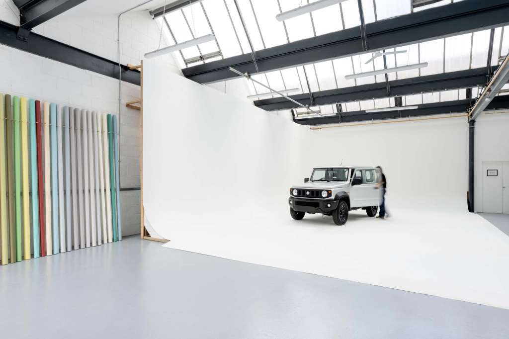 Studio space with white walls, skylights, and polished concrete floor. Vehicle displayed with colorful panel installation on left wall.