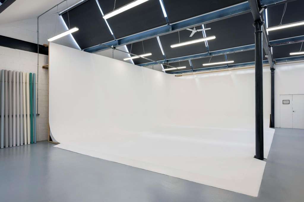Studio space with white curved wall, polished concrete floor, industrial ceiling with linear lighting, and support columns.