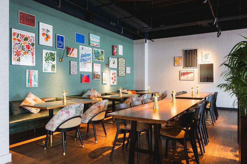 Modern dining space with teal accent wall, gallery art, wooden tables, upholstered chairs, and gold accents.