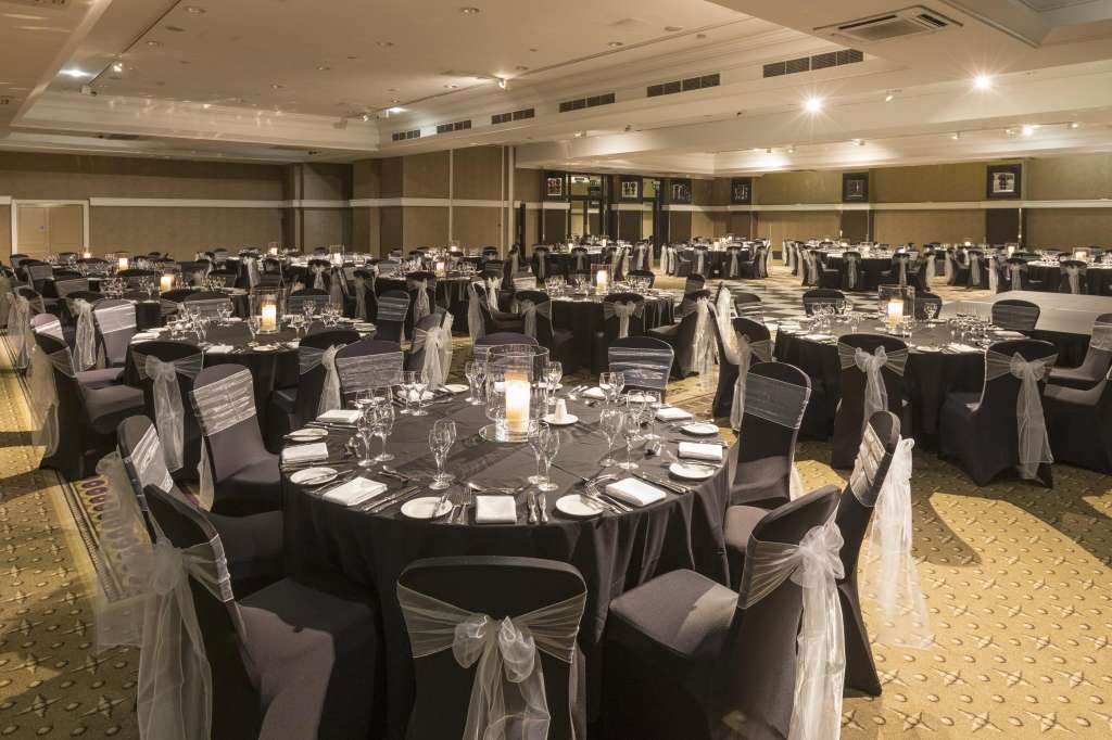 Alexandra Suite set up for a formal dinner with round tables, black linens, chair sashes, place settings, and recessed ceiling lighting.