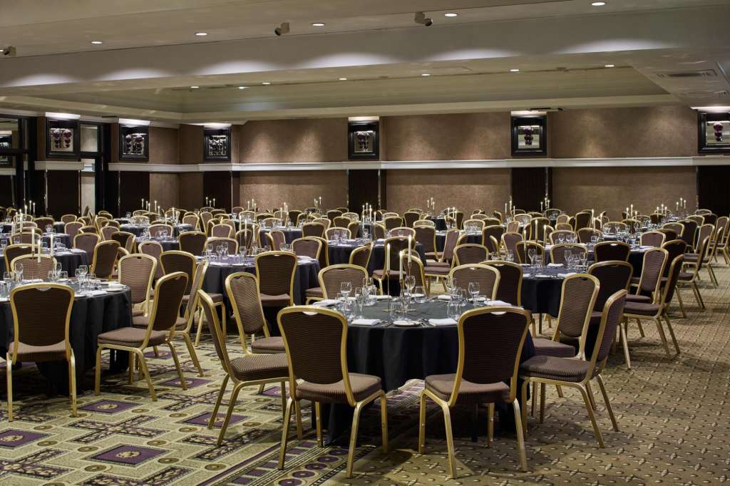 Alexandra Suite set up for a seated event with round tables, black linens, gold-framed chairs, and recessed ceiling lighting.